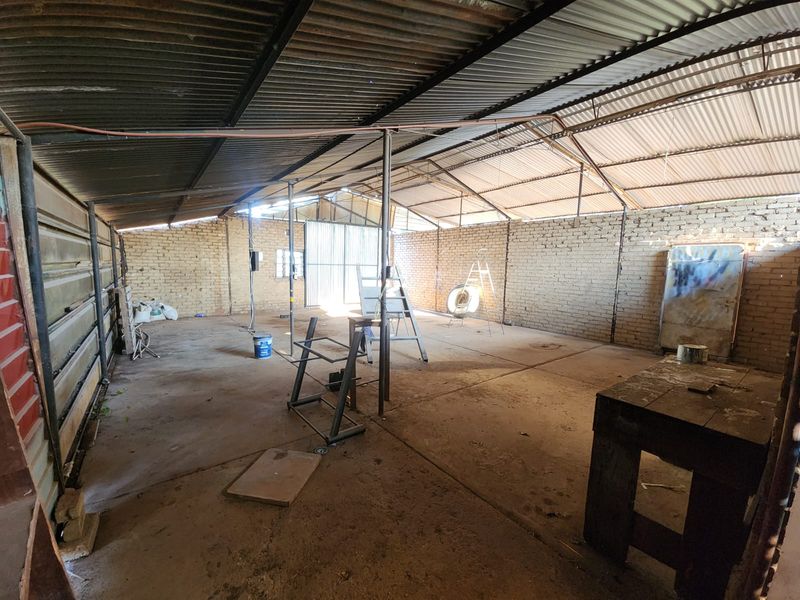 A large, open-plan industrial-style garage or workshop space featuring exposed brick walls, a corrugated metal roof, and a concrete floor.