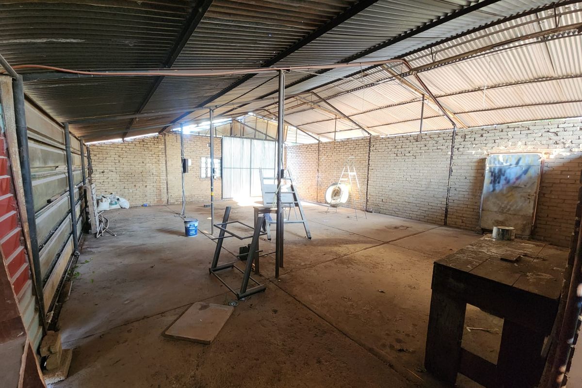 A large, open-plan industrial-style garage or workshop space featuring exposed brick walls, a corrugated metal roof, and a concrete floor.