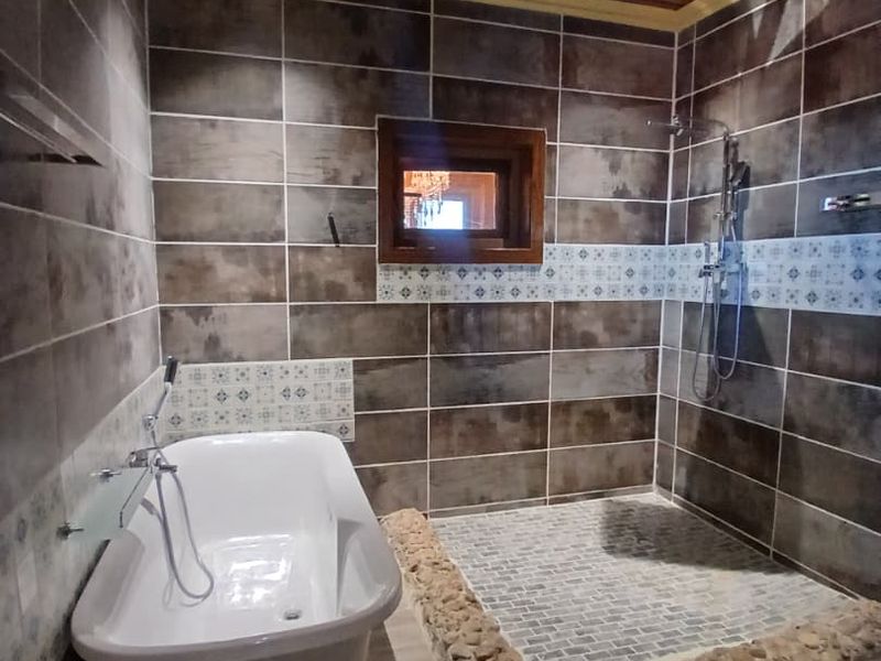 A modern bathroom featuring a freestanding bathtub, a spacious walk-in shower with a stone pebble border, and stylish tiled walls with a timber ceiling.