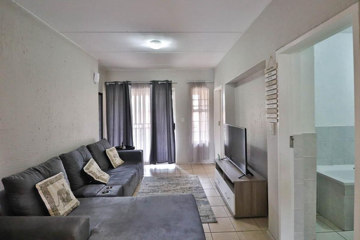 A living room featuring tiled flooring, a recessed media wall, and direct access to a balcony, with an adjacent bathroom visible.