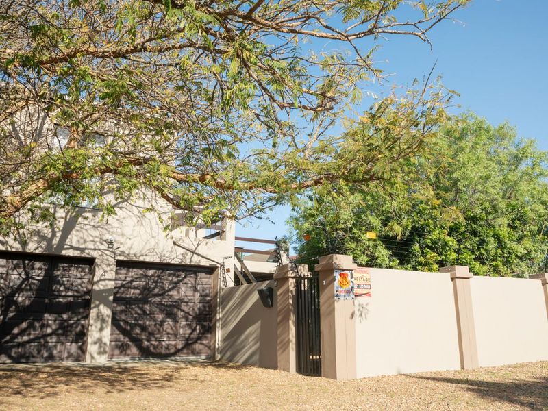 Front elevation of the apartment complex featuring a double garage, secure perimeter wall with electric fencing, and a private pedestrian entrance.