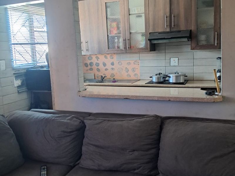 Open plan living area featuring a kitchen pass-through with built-in cabinetry, cooktop, and extractor fan, complemented by decorative ceiling detailing.