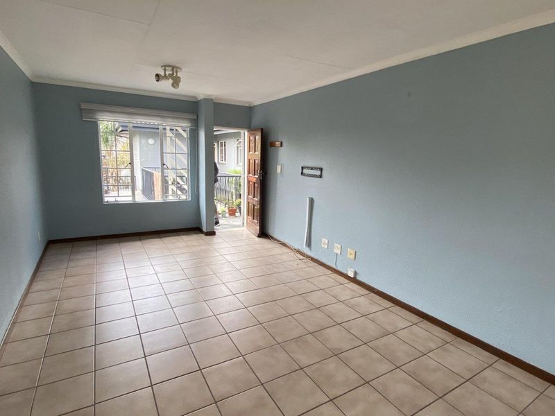 An empty, open-plan living area featuring neutral ceramic floor tiles, light blue walls, and direct access to an outdoor balcony space.