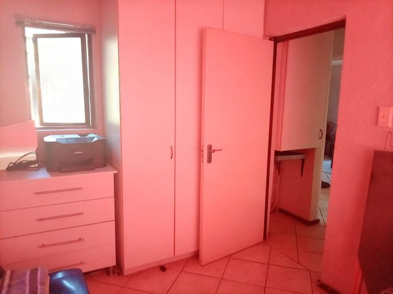 A bedroom featuring built-in cupboards, tiled flooring, and a window, showing signs of dated finishes and poor lighting conditions.