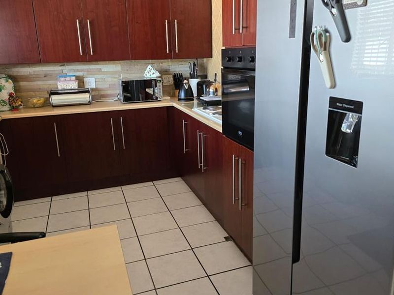 A functional kitchen featuring dark wood-finish cabinetry, laminate countertops, a tiled backsplash, and ceramic floor tiles.