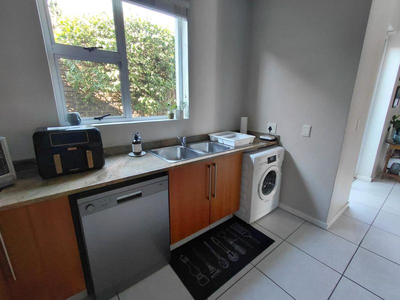 Functional laundry area featuring a double stainless steel sink, stone countertops, laminate cabinetry, and tiled flooring with space for under-counter appliances.