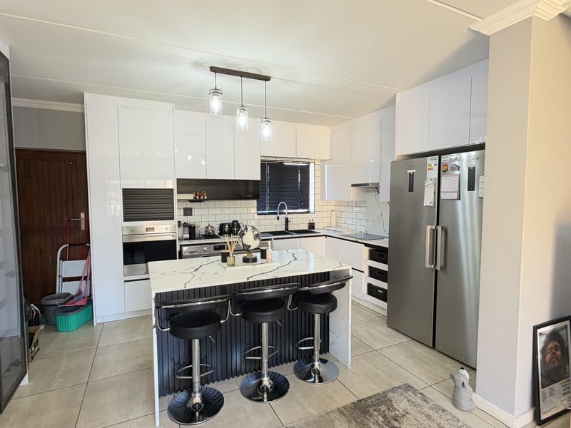 Modern kitchen featuring high-gloss white cabinetry, a central island with stone countertop, integrated appliances, and stylish subway tile backsplash.