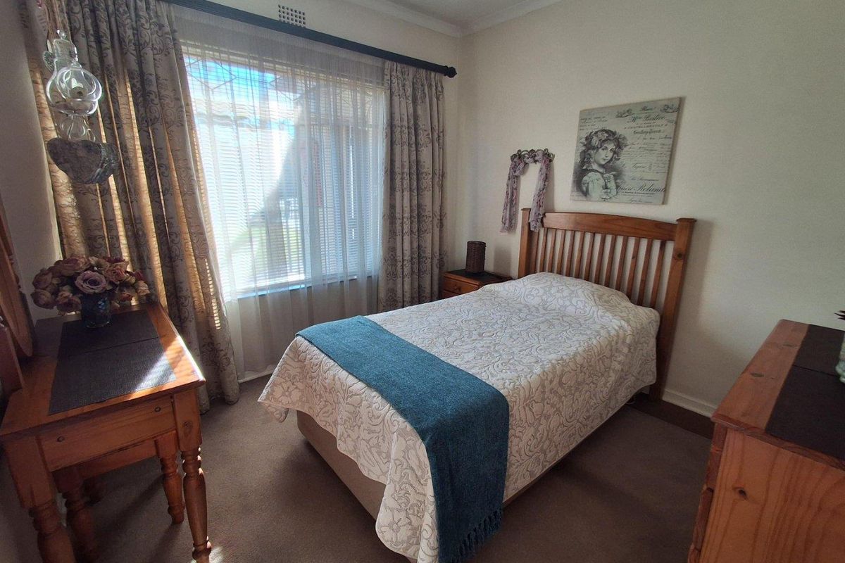A cozy bedroom featuring neutral carpeting, a large window with curtain treatments, and standard interior finishes.