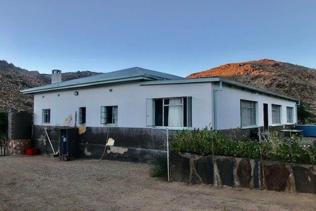 Exterior view of a farm house featuring a metal roof, stone retaining wall, and water storage tank set against a mountainous landscape.