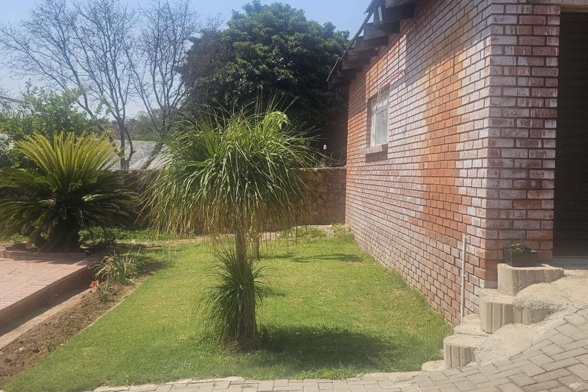 A view of the rear garden area featuring a brick exterior wall, paved patio section, and established landscaping.