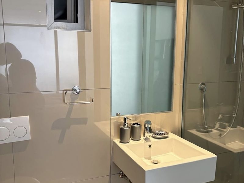Modern bathroom featuring a wall-mounted basin, glass shower enclosure, and neutral tiled finishes, providing a clean and contemporary aesthetic.