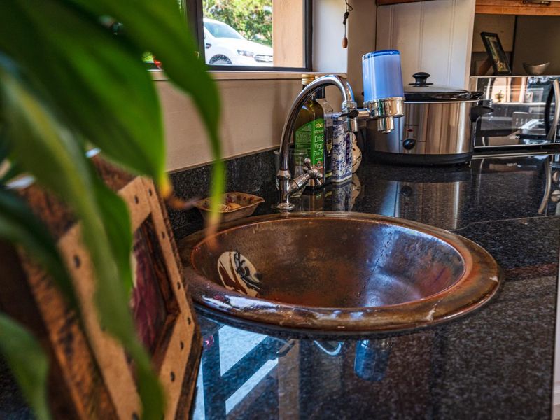 A kitchen area featuring a dark granite countertop and a unique copper basin sink with a fitted faucet and water filtration system.