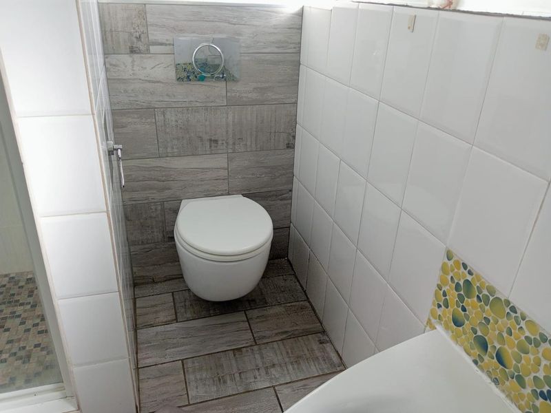 A compact bathroom featuring a wall-mounted toilet with a concealed cistern, wood-look floor tiles, and a mix of white and decorative mosaic wall tiling.