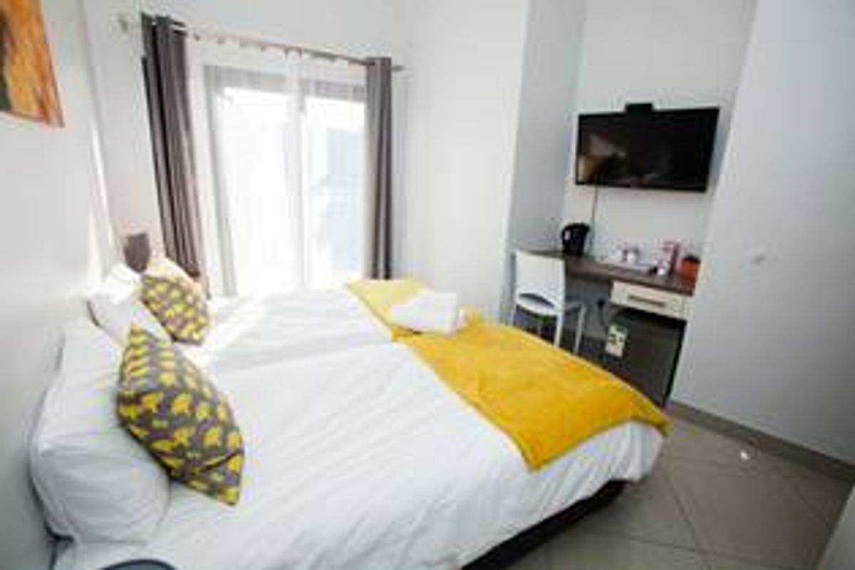 A compact bedroom featuring tiled flooring, a built-in desk area, and a sliding glass door providing natural light.
