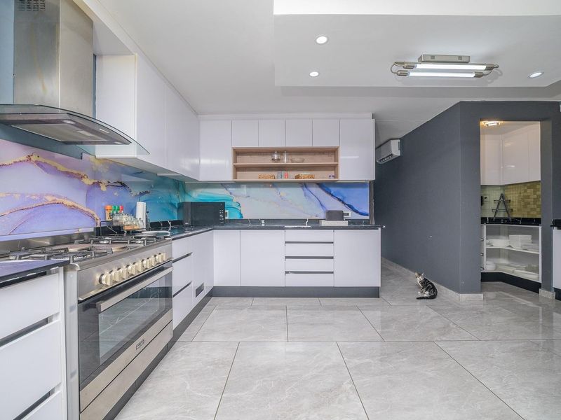 Modern kitchen featuring white cabinetry, stone countertops, a gas stove with extractor fan, and a decorative splashback, with an adjacent scullery area.