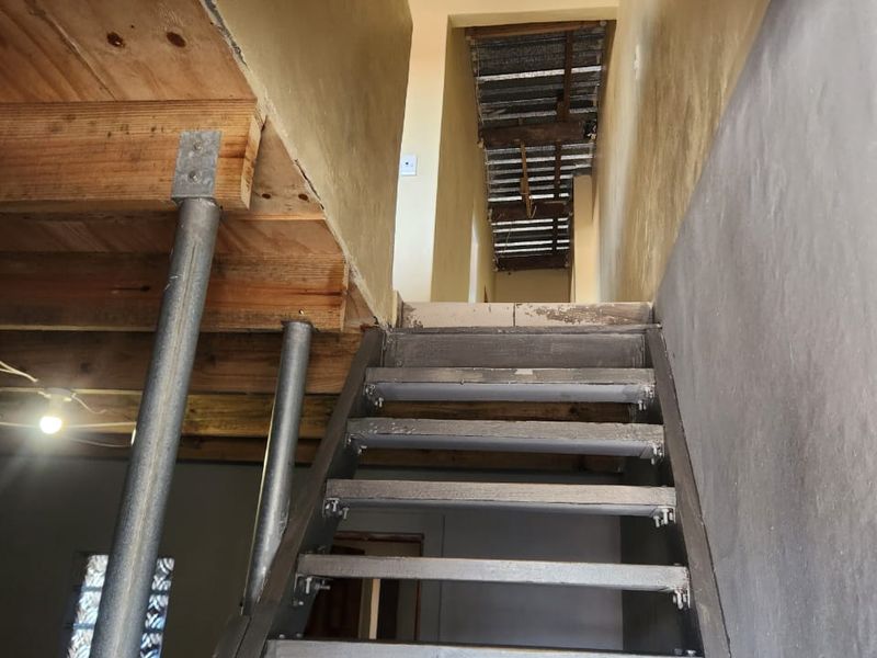 An unfinished interior space featuring a metal staircase, exposed timber joists, and steel support columns, currently in a raw construction state.