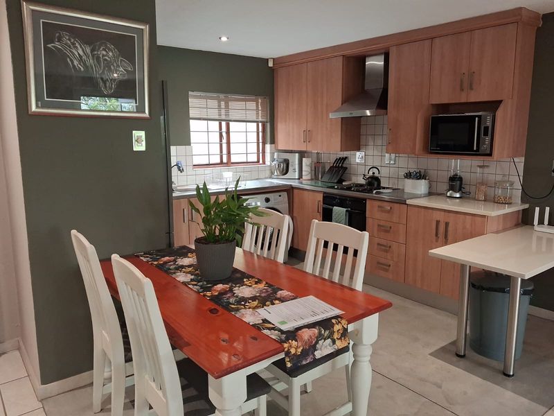 Open-plan kitchen and dining area featuring wood-finish cabinetry, built-in appliances, tiled backsplash, and neutral floor tiles.