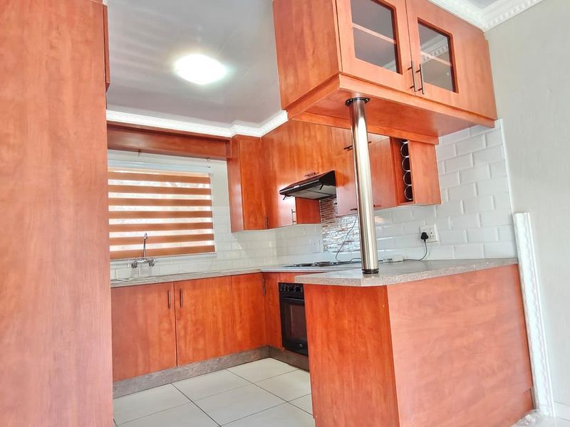 A clean, functional kitchen featuring warm-toned wooden cabinetry, subway tile backsplash, built-in oven, and a convenient breakfast bar.