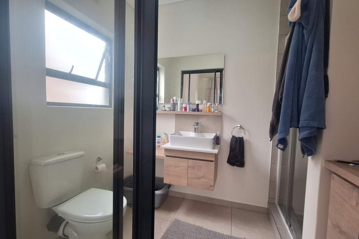 Modern bathroom featuring a floating vanity with a vessel sink, a glass shower enclosure, and a toilet, finished with neutral floor tiles.