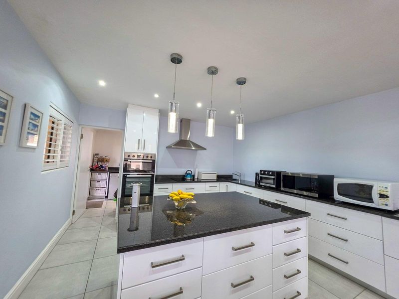Modern kitchen featuring a central island with granite countertops, white cabinetry, built-in oven, stainless steel extractor fan, and contemporary pendant lighting.