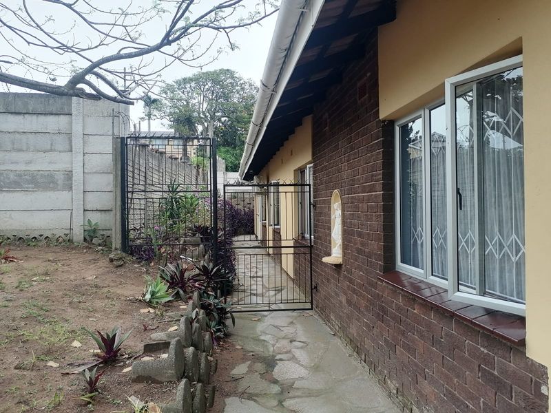 A view of the rear exterior of the house featuring a brick facade, stone pathway, and secure boundary walling.