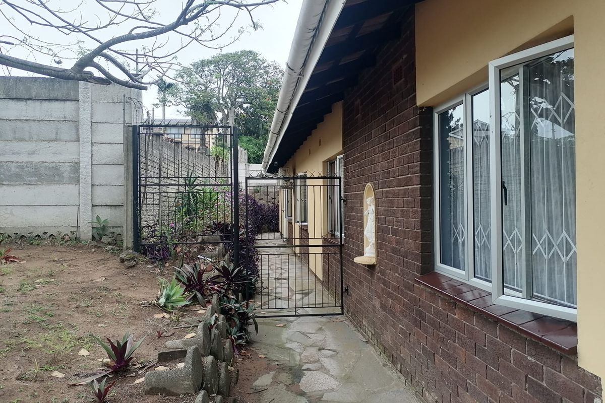 A view of the rear exterior of the house featuring a brick facade, stone pathway, and secure boundary walling.