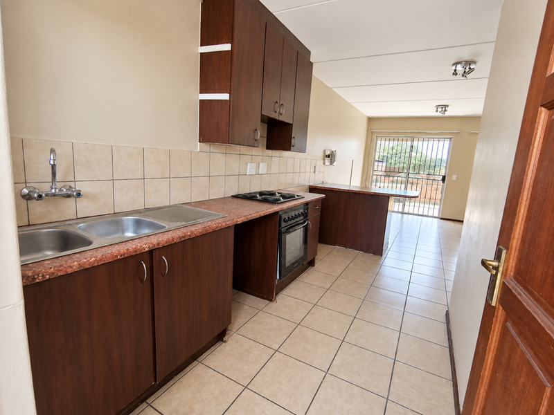 Open-plan kitchen featuring dark wood cabinetry, laminate countertops, built-in oven and hob, and tiled flooring leading to a rear sliding door.