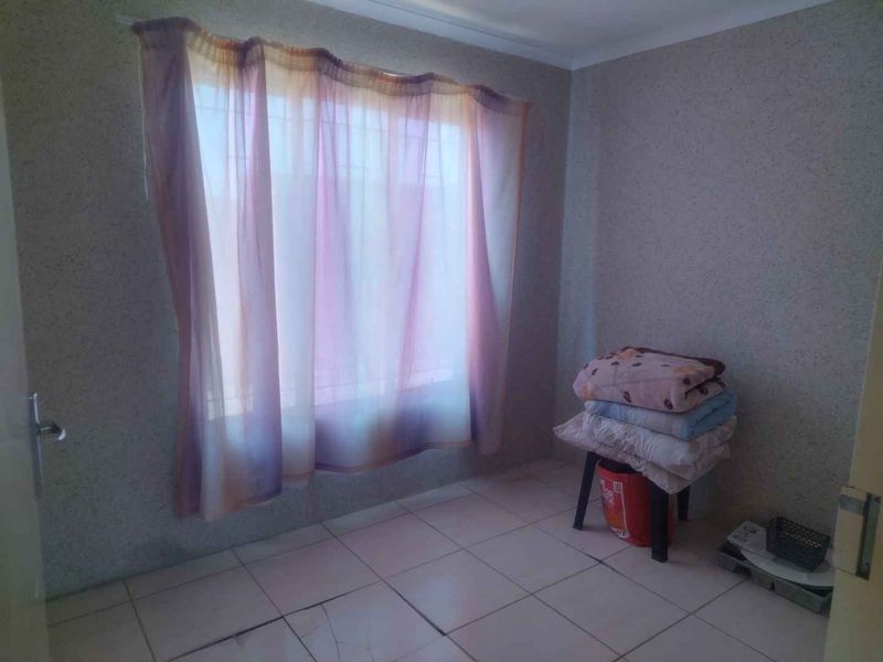 A simple bedroom featuring tiled flooring and a window with security bars, currently vacant and ready for updates.