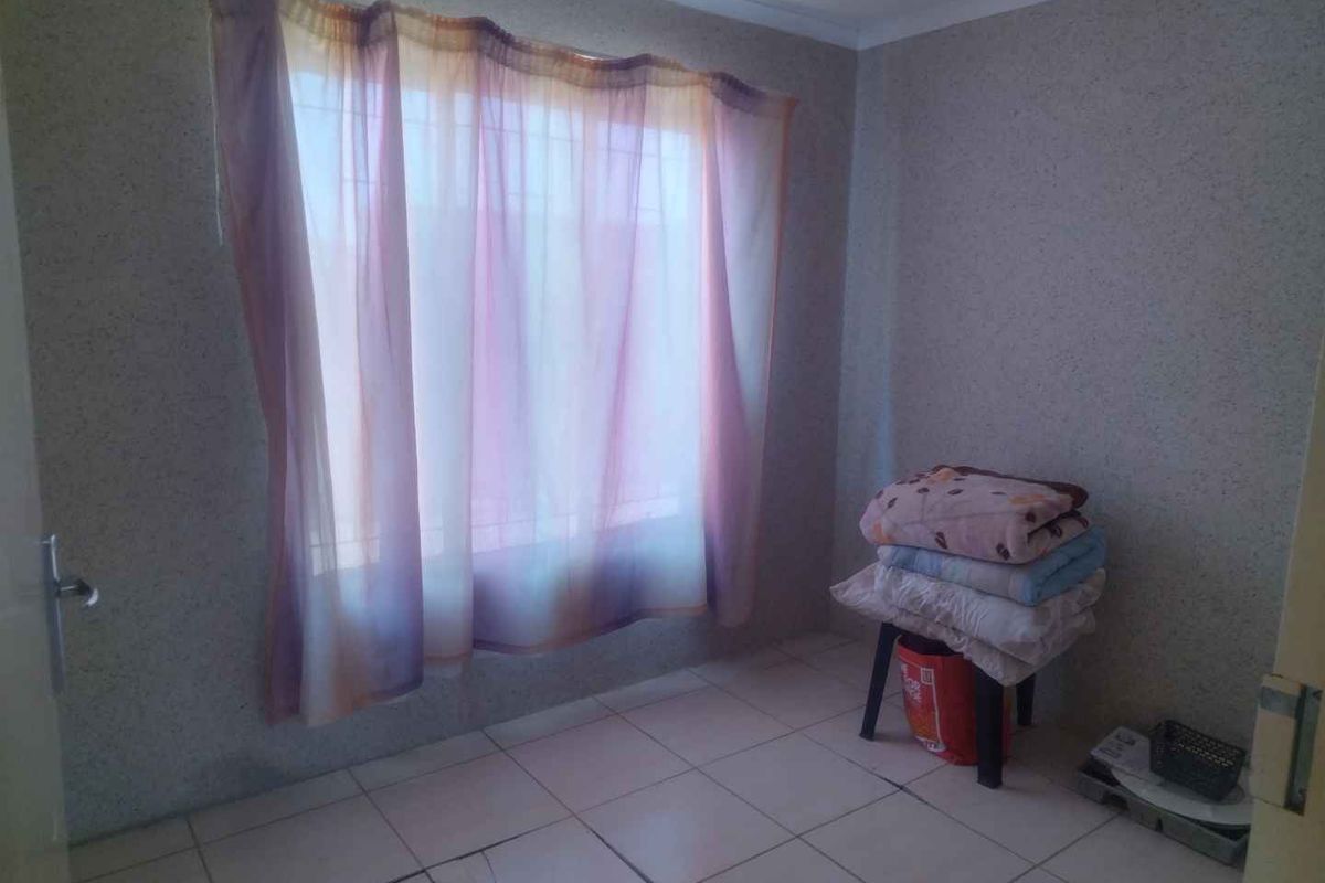 A simple bedroom featuring tiled flooring and a window with security bars, currently vacant and ready for updates.