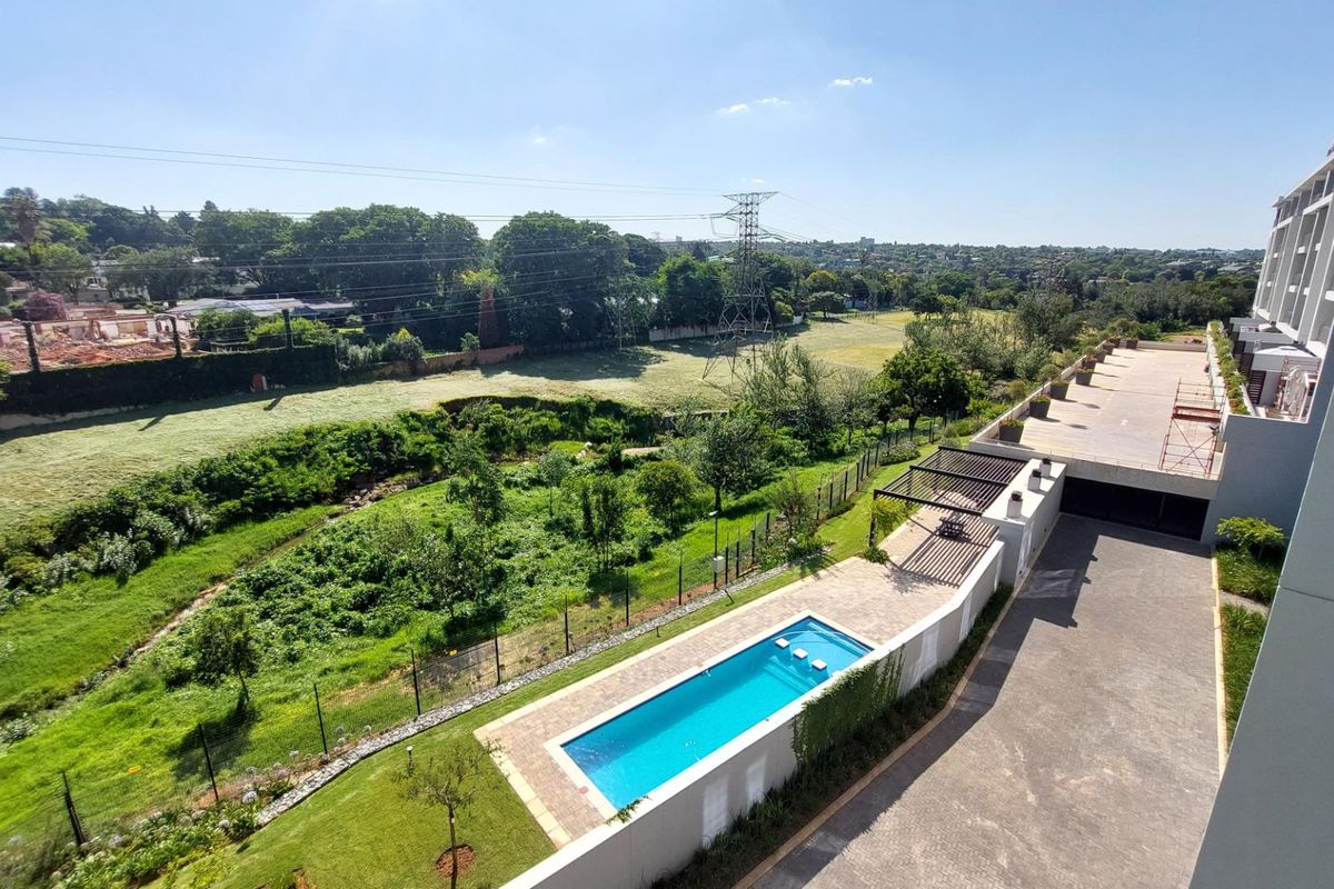 Aerial view of the apartment complex grounds featuring a swimming pool, paved patio area with pergola, and surrounding landscaped garden space.