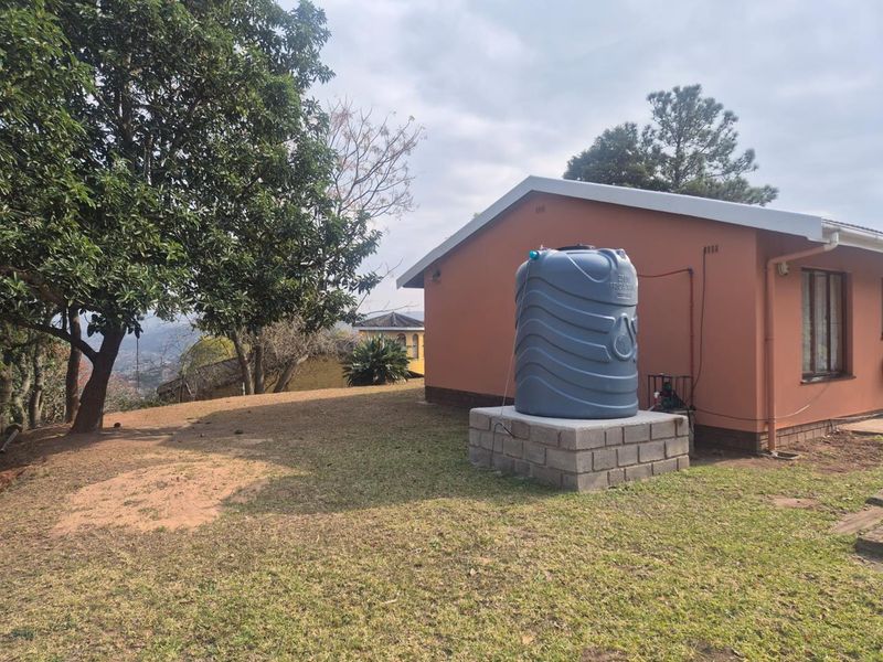 Rear exterior view of the property featuring a water storage tank mounted on a concrete block plinth with an integrated pump system.