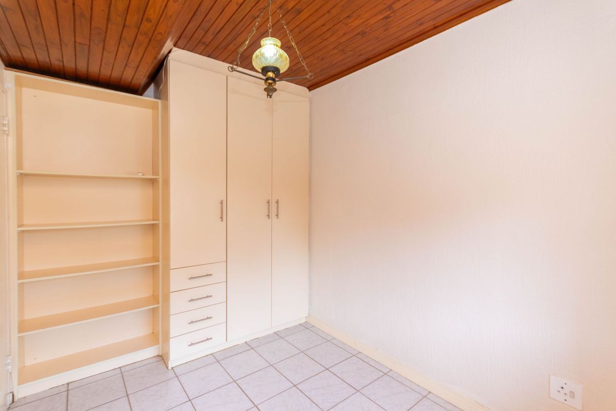 A bedroom featuring built-in cabinetry with integrated shelving and drawers, finished with a timber-paneled ceiling and tiled flooring.