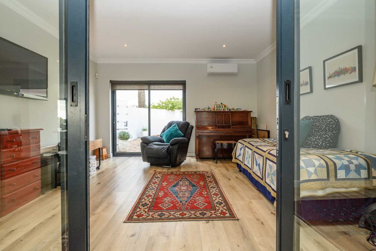 A bright bedroom featuring light wood-look flooring, recessed ceiling lighting, a wall-mounted air conditioning unit, and sliding glass doors leading to an outdoor area.