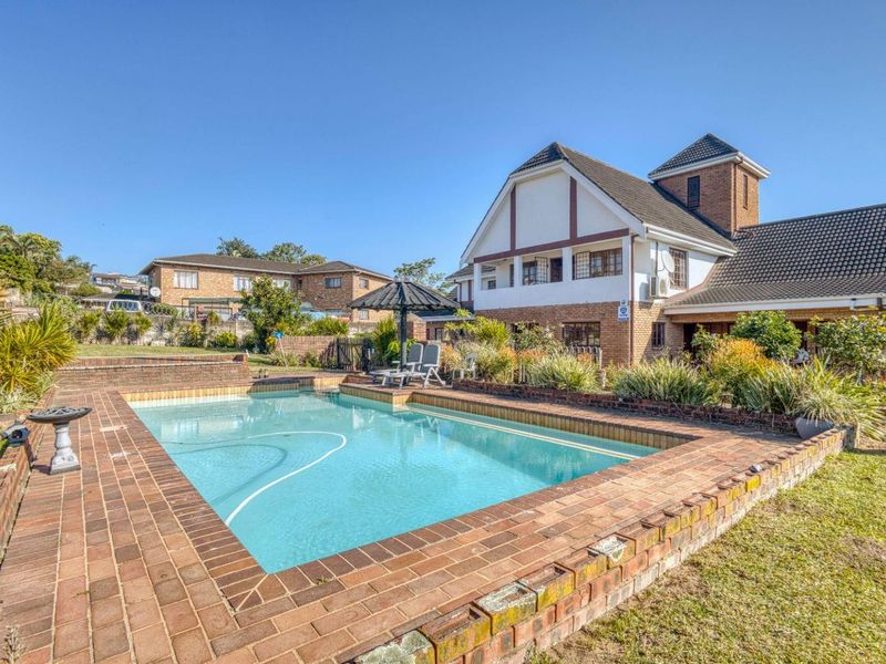 A well-maintained outdoor pool area featuring brick paving and coping, set against the rear elevation of a multi-story residential house.