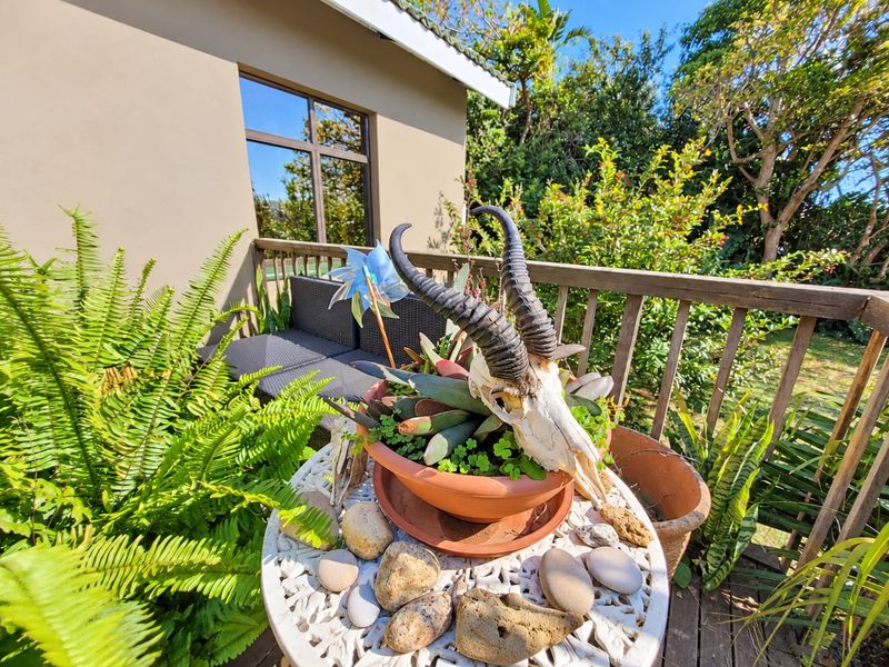 A sunny outdoor wooden deck area featuring a balustrade and views of the surrounding garden.