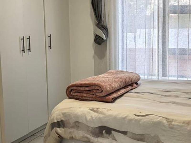 A neat bedroom featuring tiled flooring, built-in cupboards, and recessed ceiling lighting, providing a functional and well-maintained living space.