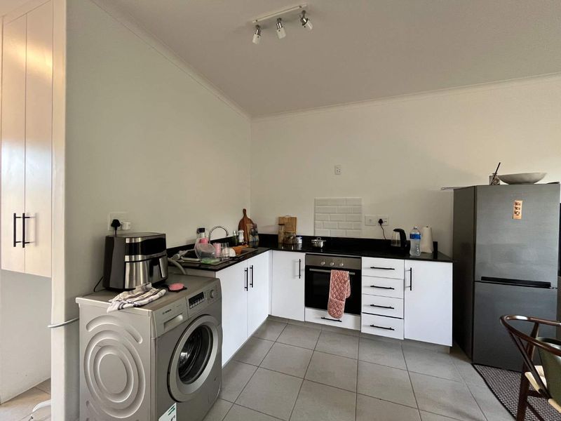 A functional kitchen featuring white cabinetry, dark countertops, a subway tile backsplash, and integrated oven and hob, with tiled flooring throughout.