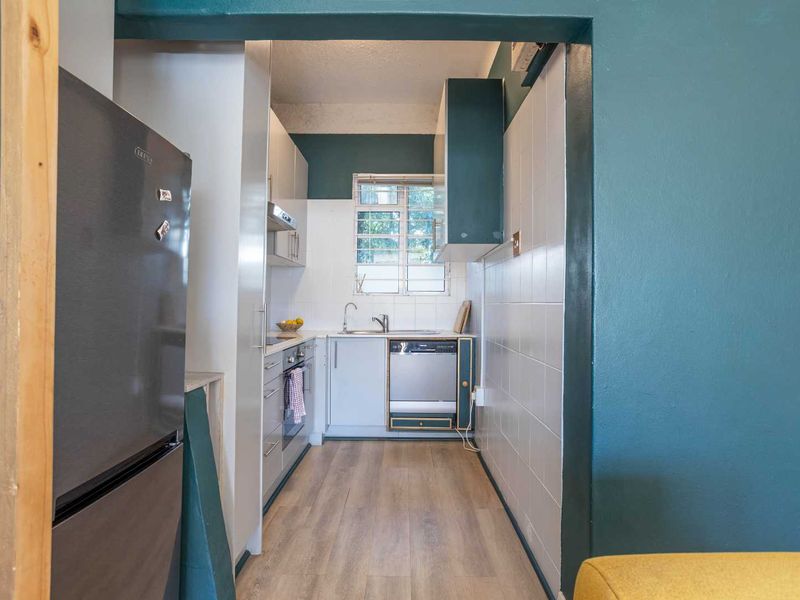 Compact galley-style kitchen featuring built-in cabinetry, tiled backsplash, and integrated appliances, providing a functional workspace with a neutral aesthetic.