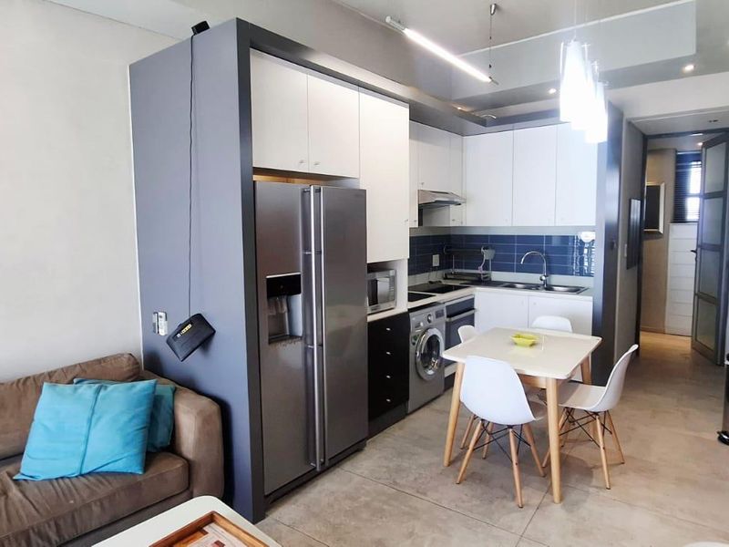 Modern open-plan apartment featuring a compact kitchen with built-in cabinetry, integrated appliances, and tiled flooring, seamlessly flowing into the living area.