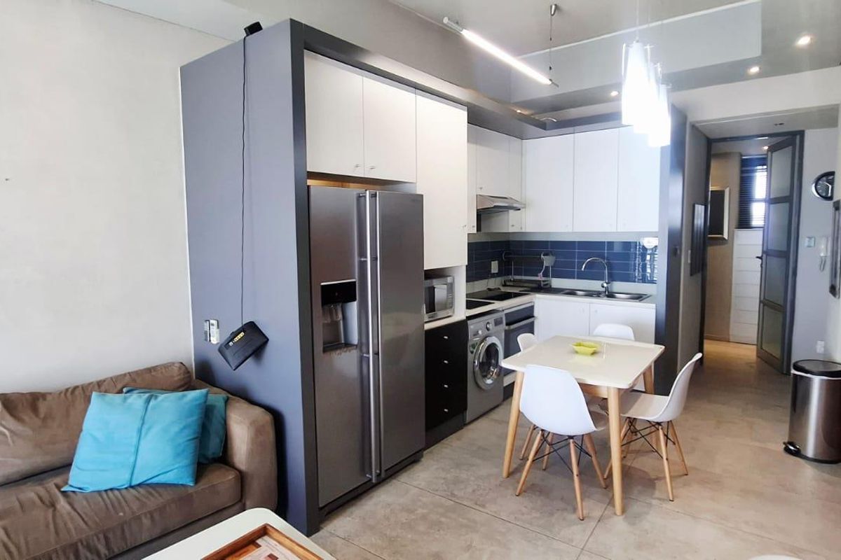 Modern open-plan apartment featuring a compact kitchen with built-in cabinetry, integrated appliances, and tiled flooring, seamlessly flowing into the living area.