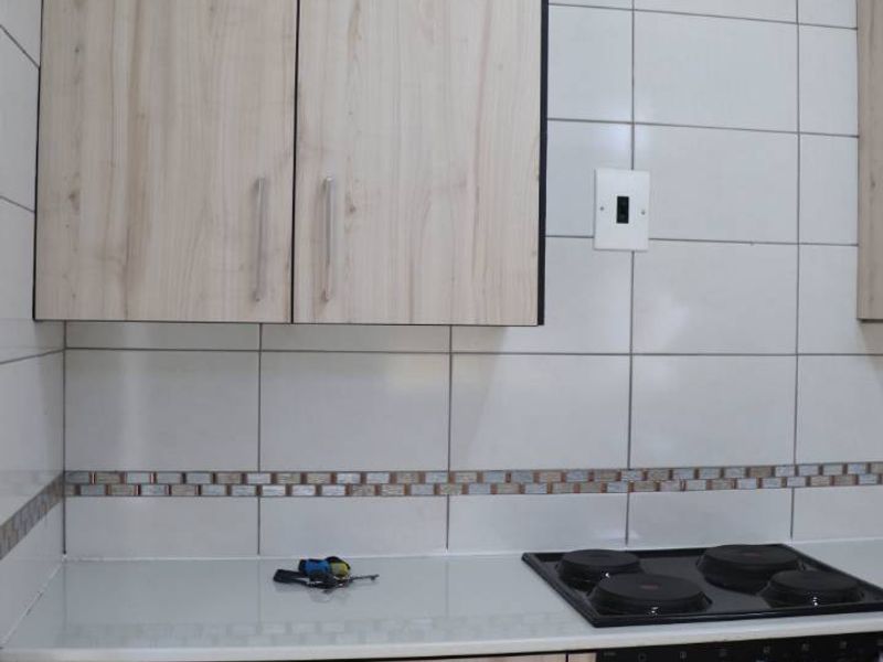 A modern kitchen area featuring light wood-finish cabinetry, a built-in electric oven and hob, and a clean tiled backsplash.