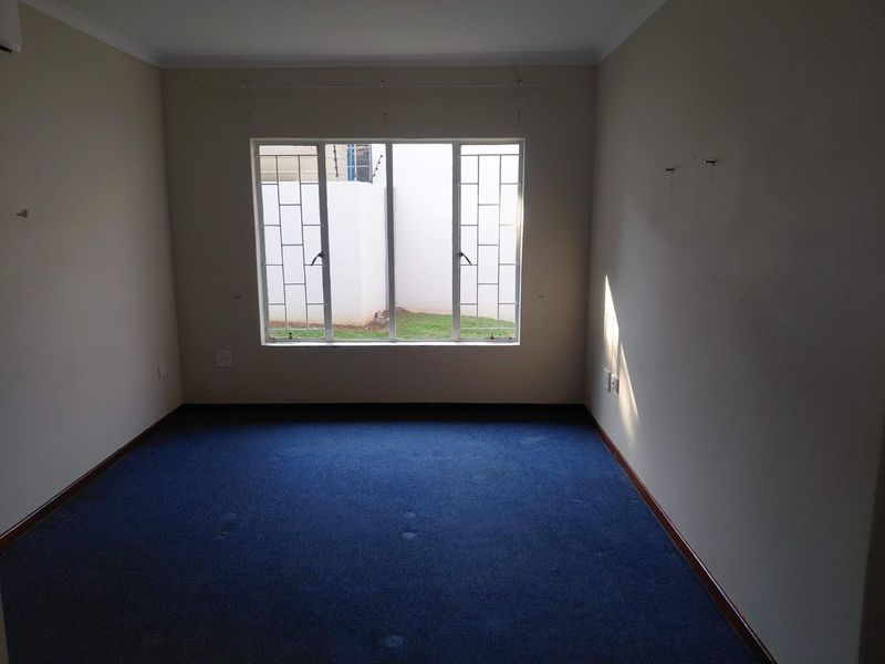 An empty bedroom featuring blue carpeting, neutral walls, and a window fitted with security bars.