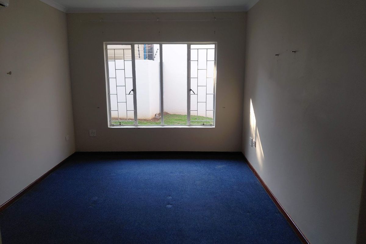 An empty bedroom featuring blue carpeting, neutral walls, and a window fitted with security bars.