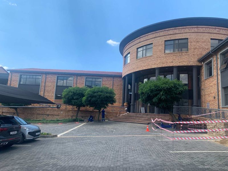 Front exterior view of a modern brick office building featuring a circular architectural design, paved parking area, and covered entrance.