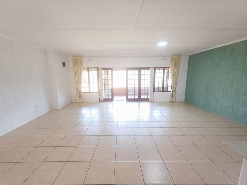 Spacious, empty living area featuring neutral tiled flooring, an accent wall, and large french doors providing access to the outdoor space.
