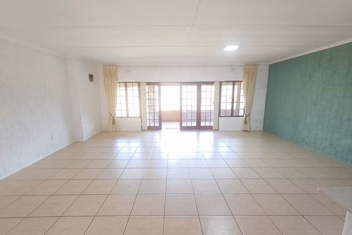 Spacious, empty living area featuring neutral tiled flooring, an accent wall, and large french doors providing access to the outdoor space.