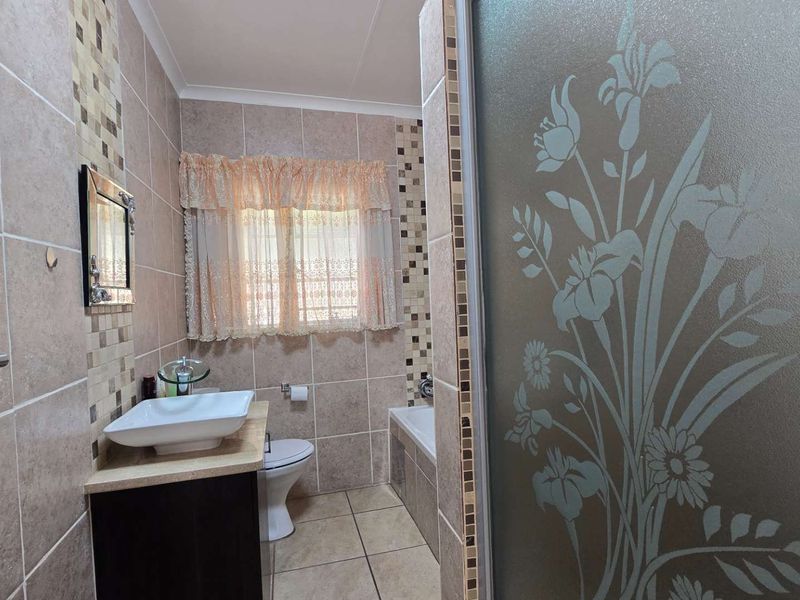A functional bathroom featuring a vessel sink, vanity cabinet, toilet, and a bathtub with tiled finishes and a decorative frosted glass shower door.