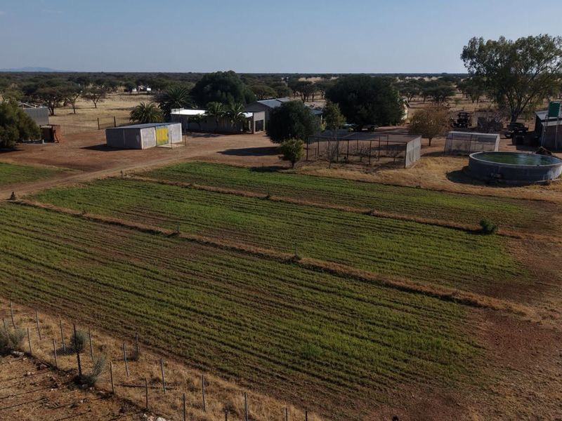 Aerial view of a farm property featuring cultivated fields, multiple outbuildings, and a circular water reservoir.