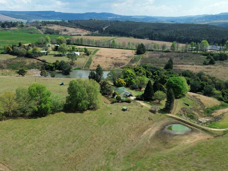 Aerial view of a sprawling farm property featuring open pastures, a private dam, and established trees set against a scenic landscape.