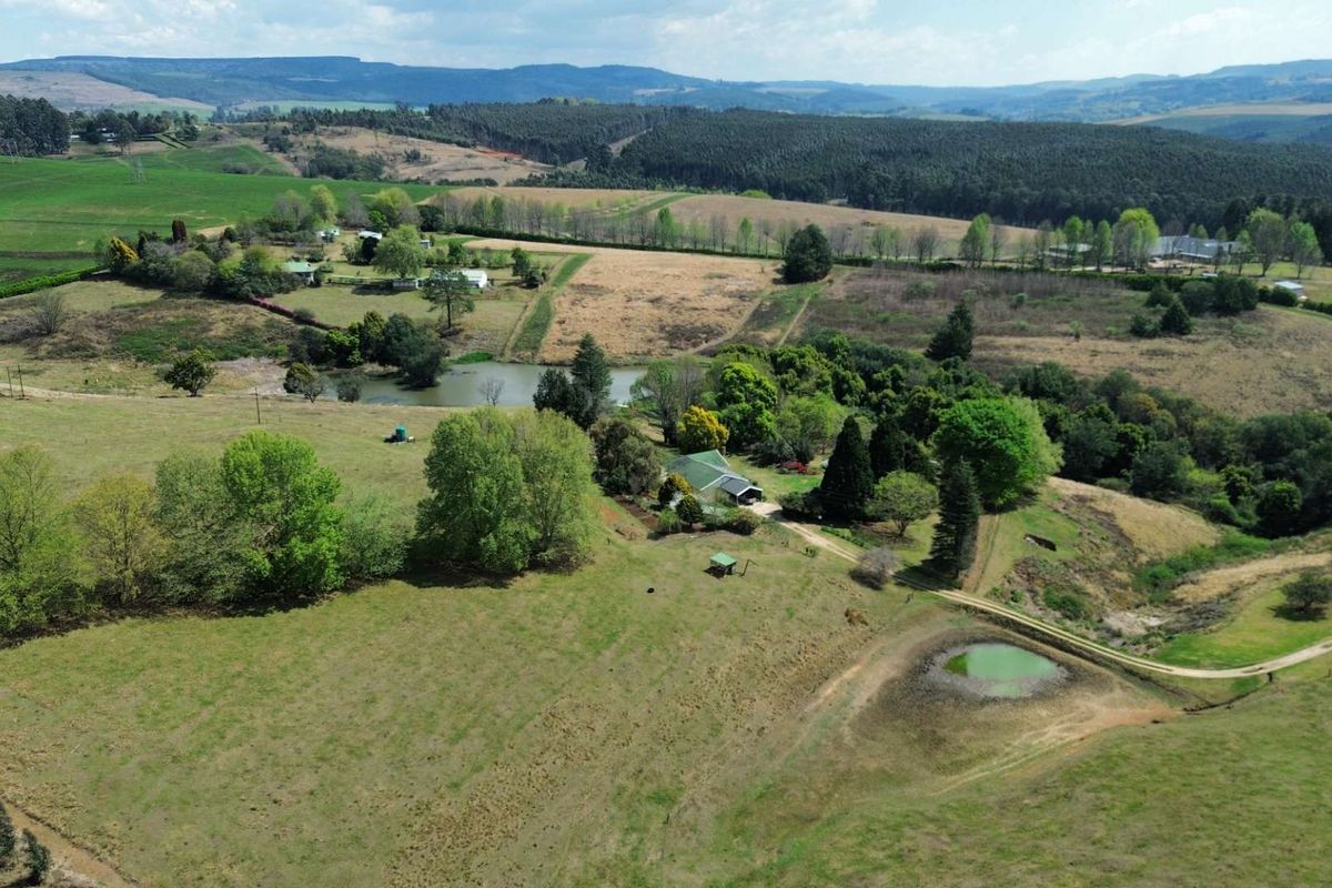 Aerial view of a sprawling farm property featuring open pastures, a private dam, and established trees set against a scenic landscape.